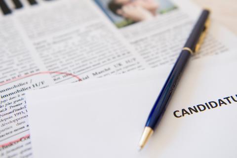 extrait d'un journal avec une offre d'emploi entourée de rouge, un stylo et une feuille sur laquelle est noté le mot candidature