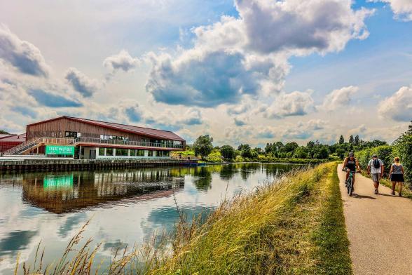 chemin au bord de l'eau, de l'autre côté un bâtiment est présent en bordure d'eau - Agrandir l'image, fenêtre modale